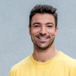 Ramon Babazadeh Biografie: Porträtfoto des deutschen TV-Moderators in gelbem Pullover mit einem offenen, sympathischen Lächeln vor grauem Hintergrund.